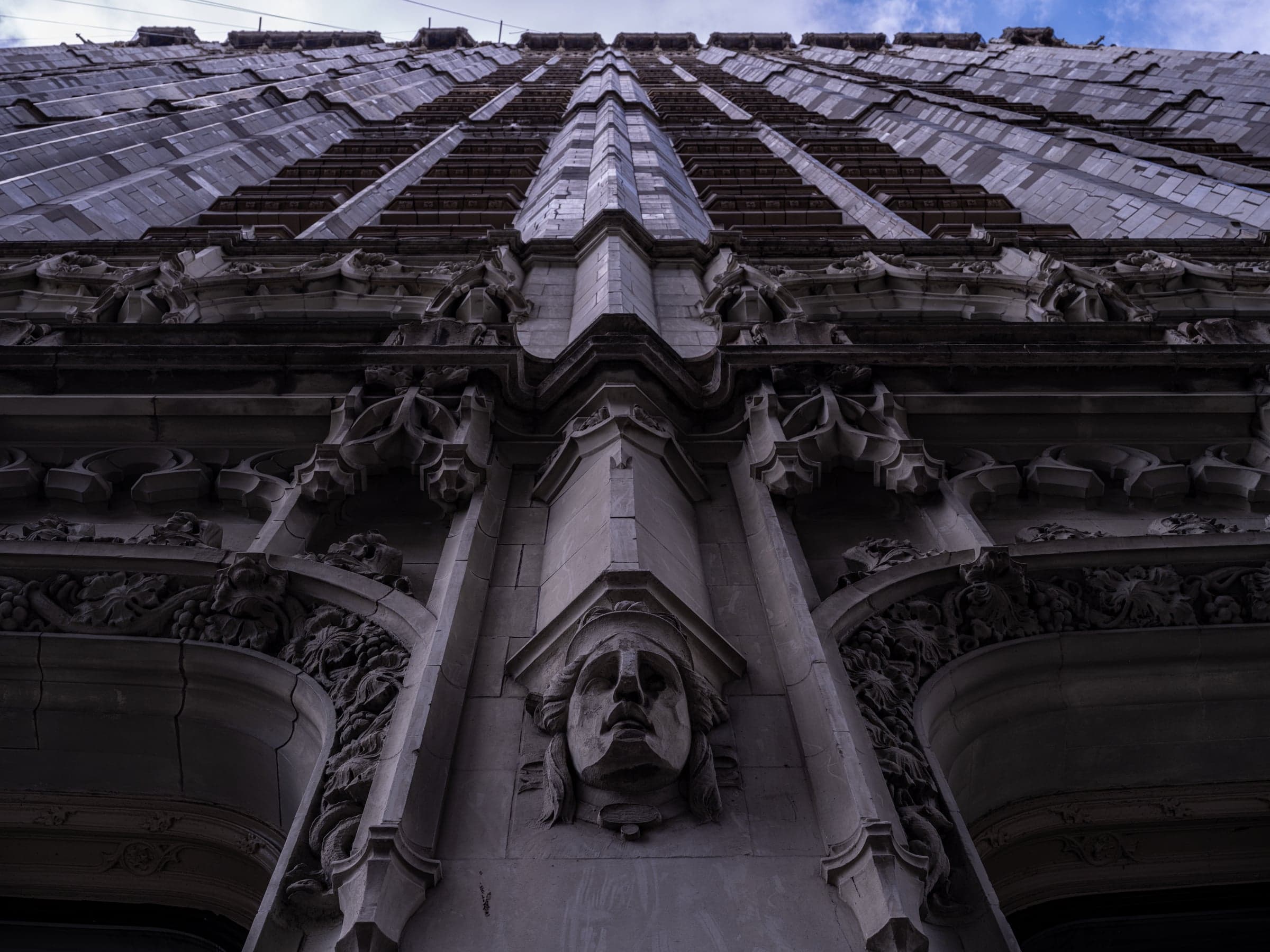 Dark upward view of the Woolworth Building's Gothic ornament and carved face at the cornice line.