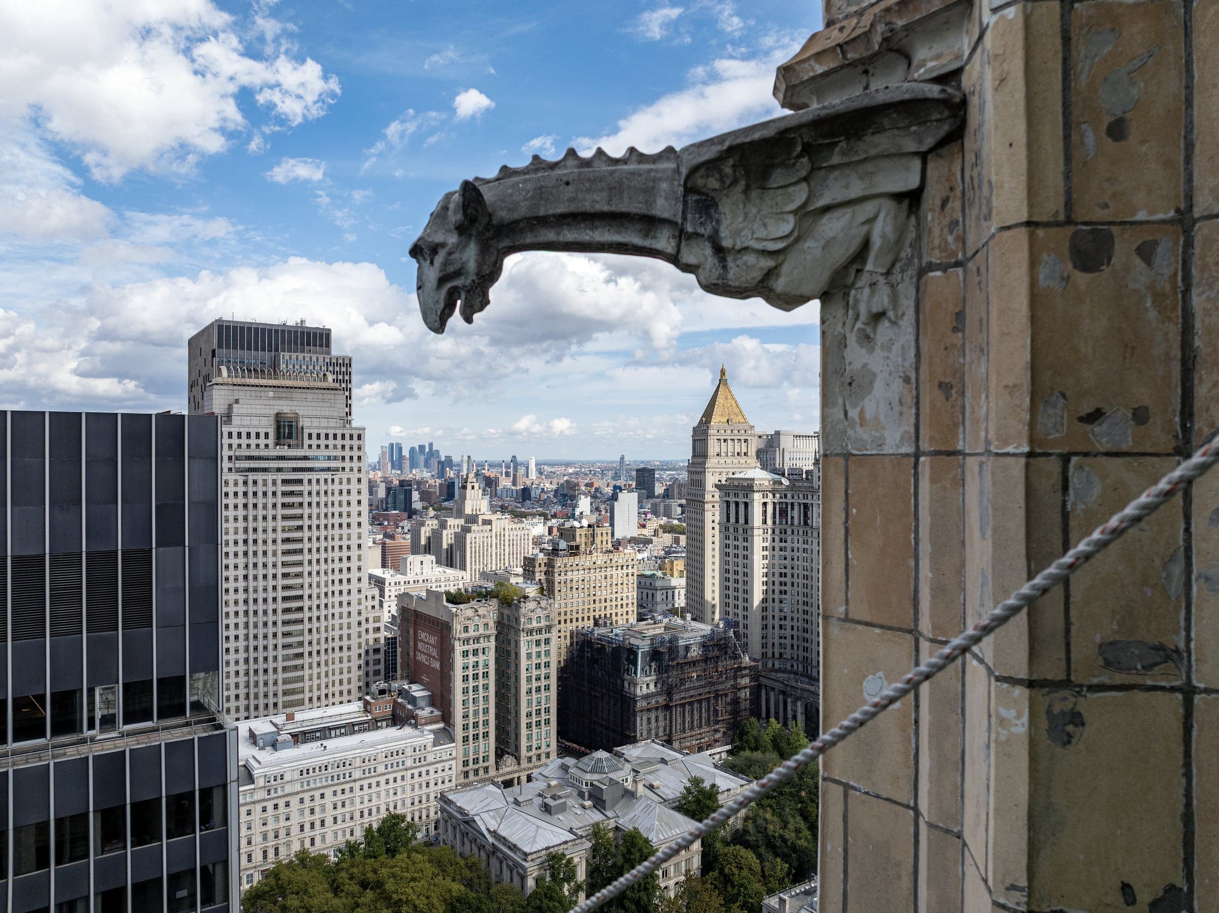 A Gothic gargoyle sculpture on the upper tower of the Woolworth Building with the Manhattan skyline behind.