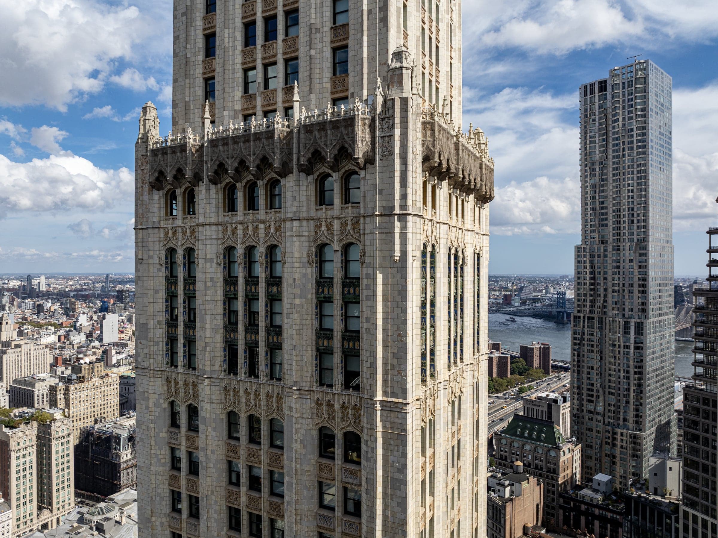 Three-quarter view of the Woolworth Building's upper tower and crown from a nearby vantage, with the city and river beyond.